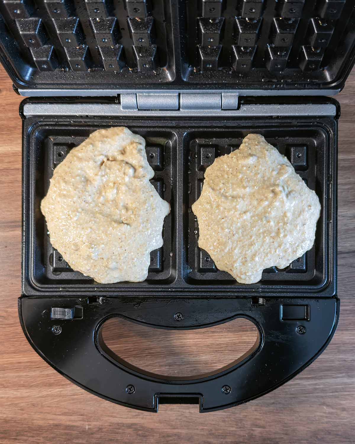 An open waffle maker with waffle batter in it.