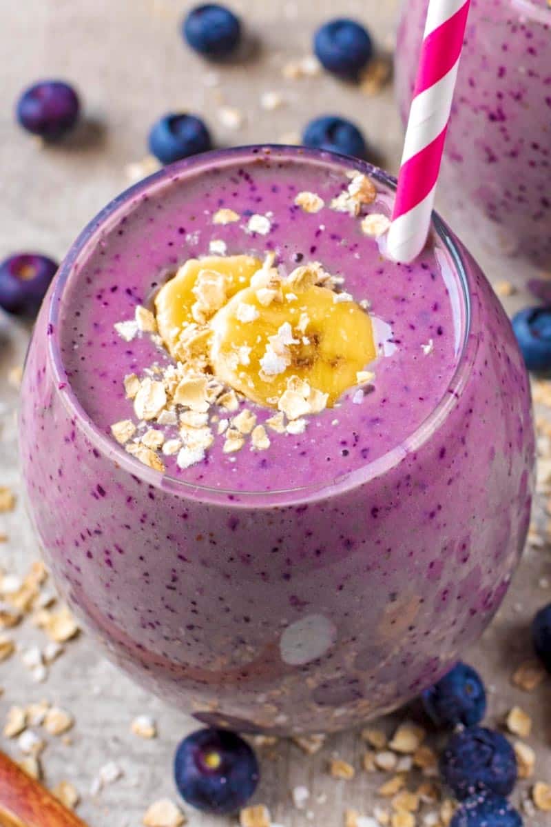 A purple coloured smoothie topped with sliced banana and oats.