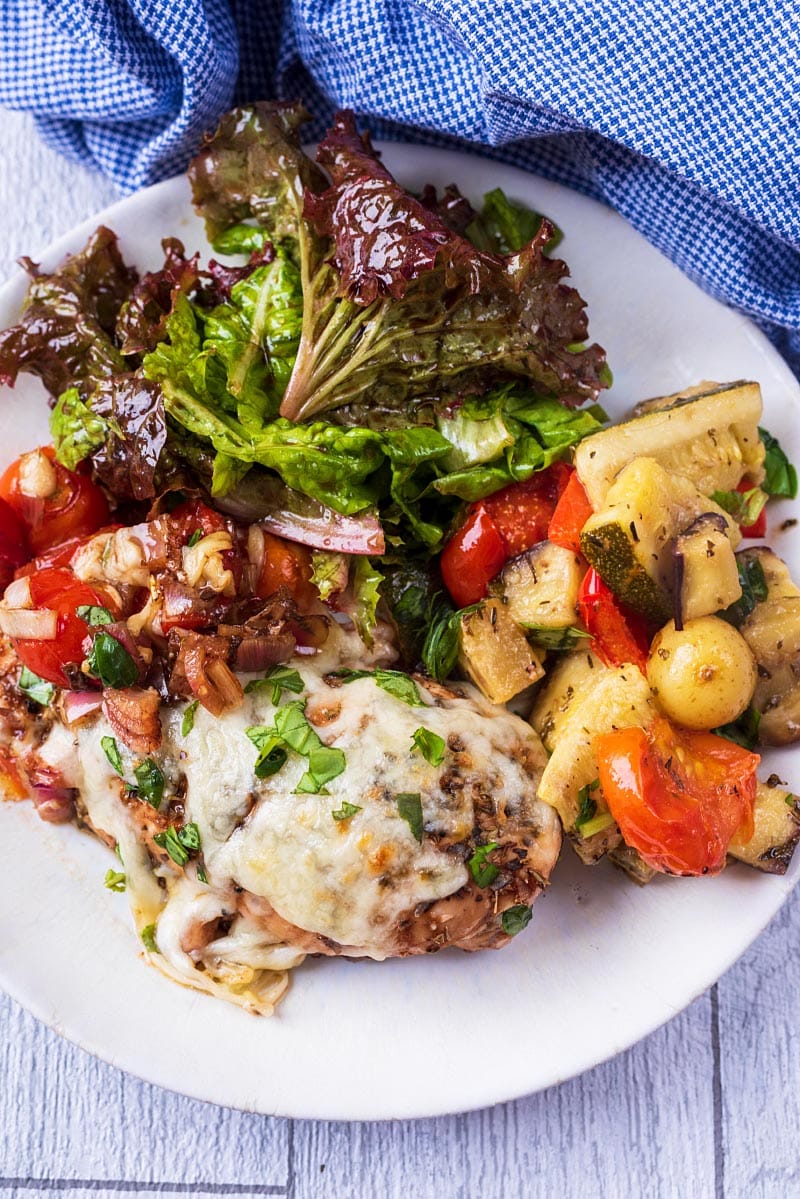 A plate of Caprese Chicken, salad and vegetables.