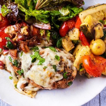 Caprese chicken on a plate with roastred vegetables and some salad leaves