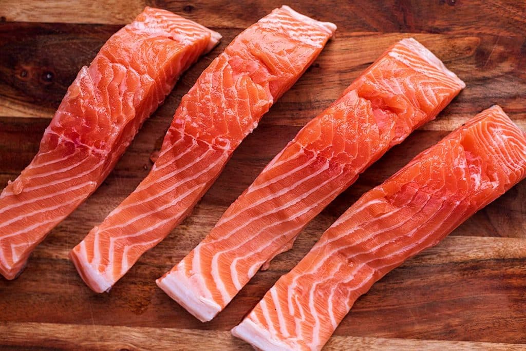 Four uncooked salmon fillets on a wooden chopping board