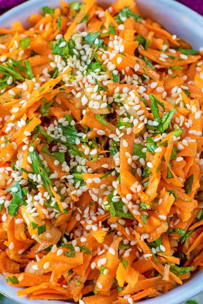 A bowl of grated carrot with herbs and sesame seeds.