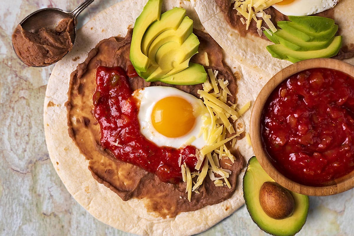 Huevos Rancheros topped with sliced avocado and grated cheese.