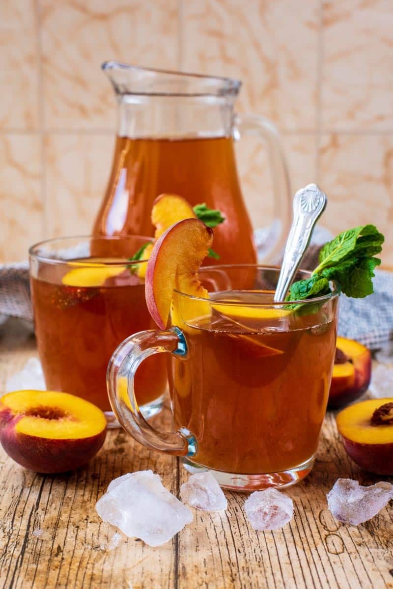 A glass of Peach Iced Tea in front of a jug of more iced tea.