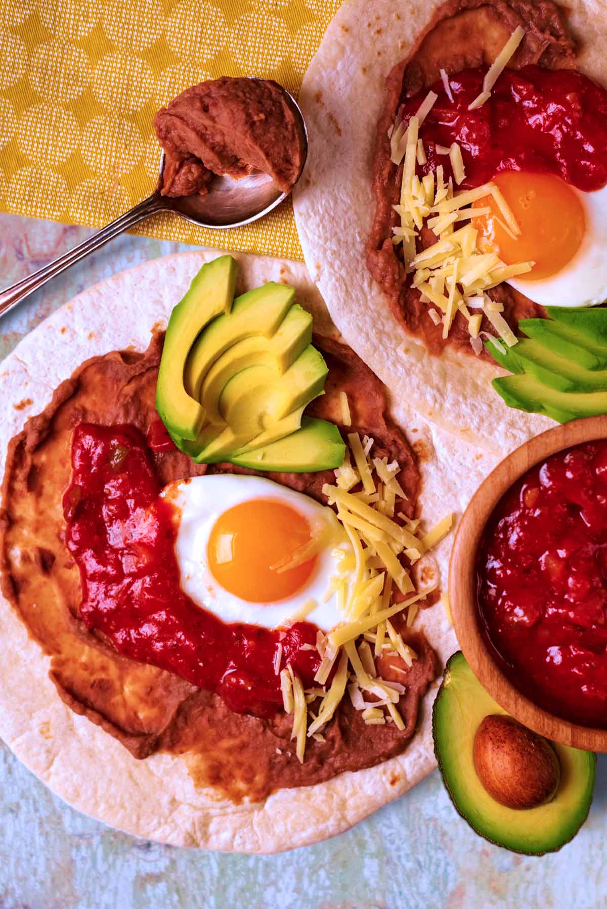 Huevos Rancheros on a marble surface with a bowl of salsa and half an avocado.