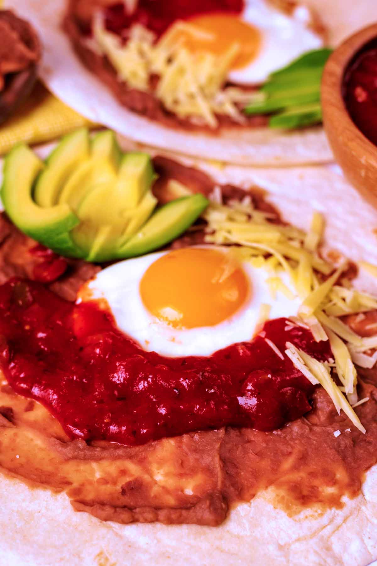 Huevos Rancheros with cheese and sliced avocado in front of another portion.