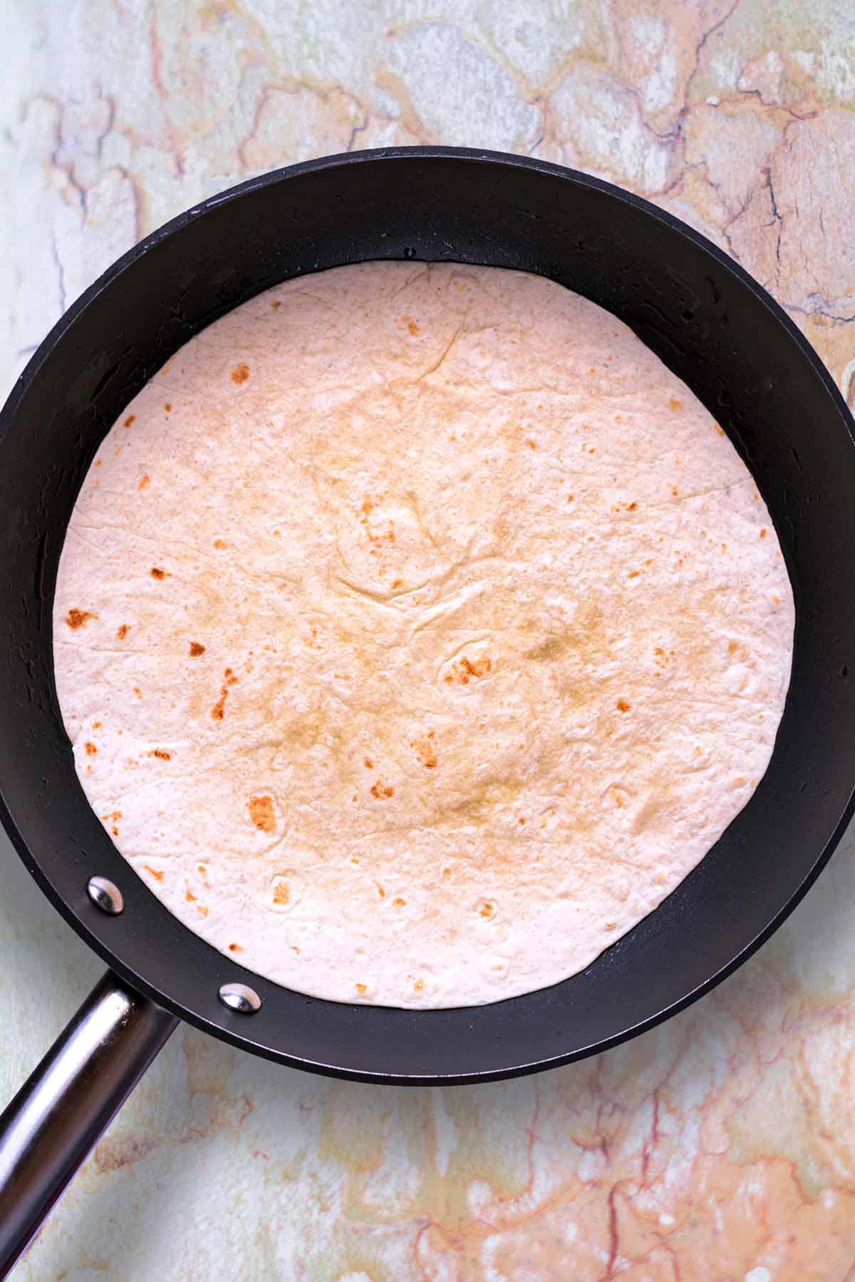 A frying pan with a flour tortilla being heated in it.