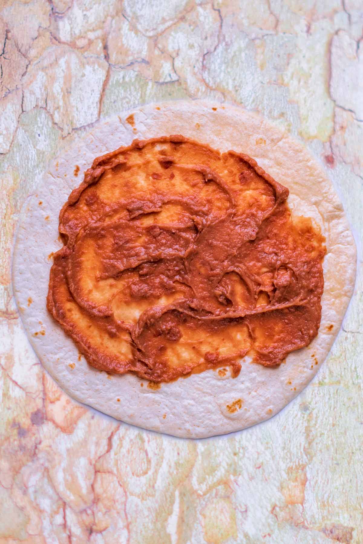 A tortilla wrap with refried beans spread over it.