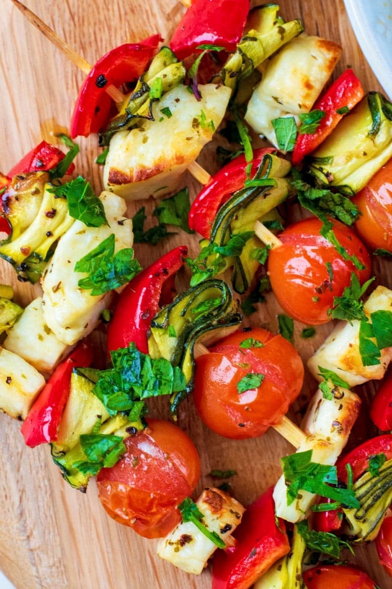 Vegetables and cubes of halloumi on wooden skewers.