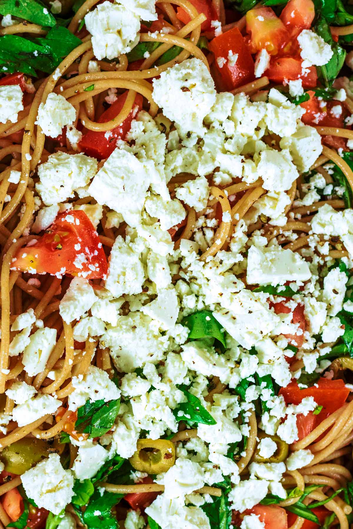 Crumbled feta on top of spaghetti, tomatoes, olives and basil.