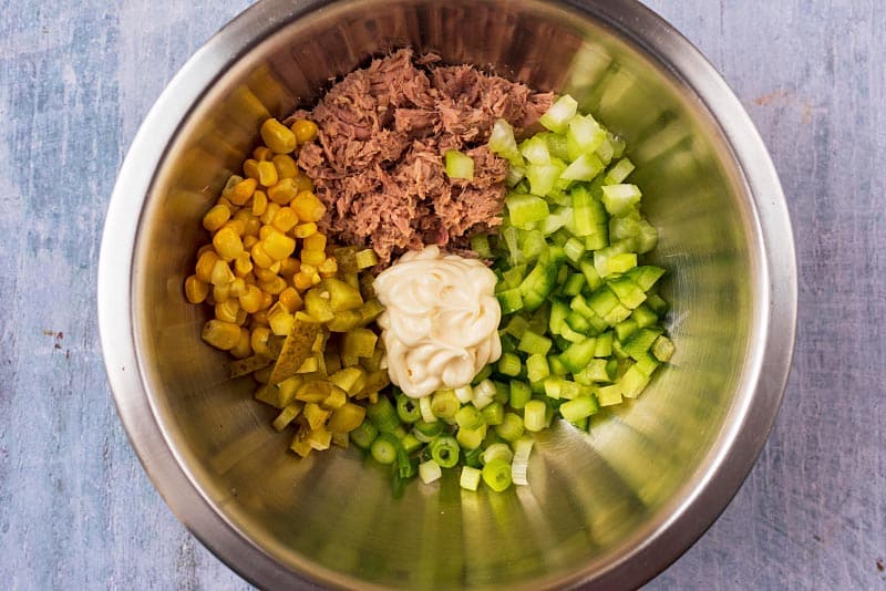 A metal mixing bowl filled with tuna, onion, sweetcorn, gherkins and mayonaise.