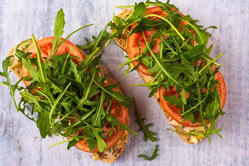 Two slices of bread topped with tuna, salad, tomatoes and arugula.