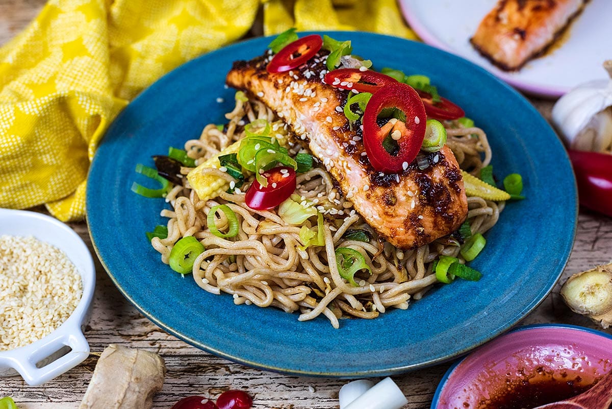 Noodles and salmon on a plate topped with chillies and spring onions.