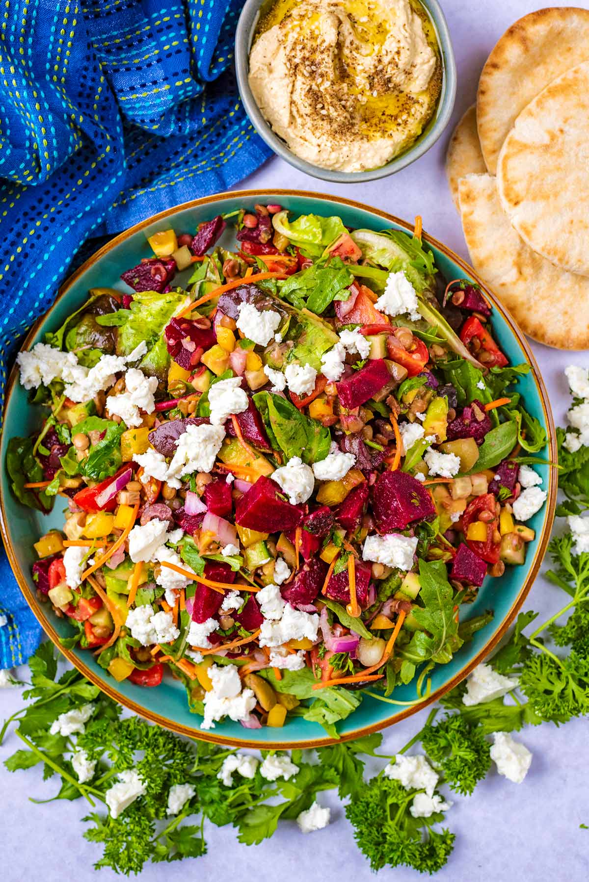 A large bowl of salad next to some hummus and pita breads.