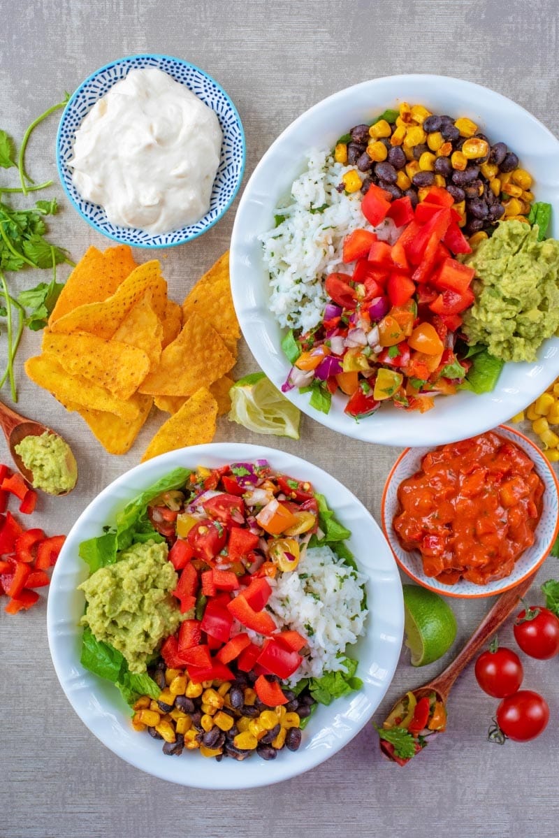 Two burrito bowls surrounded by ingredients.