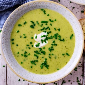 A bowl of creamy courgette soup next to two slices of bread.