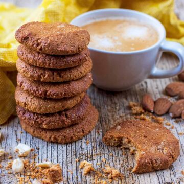 A stack of healthy gingernut biscuits in front of a cup of coffee.