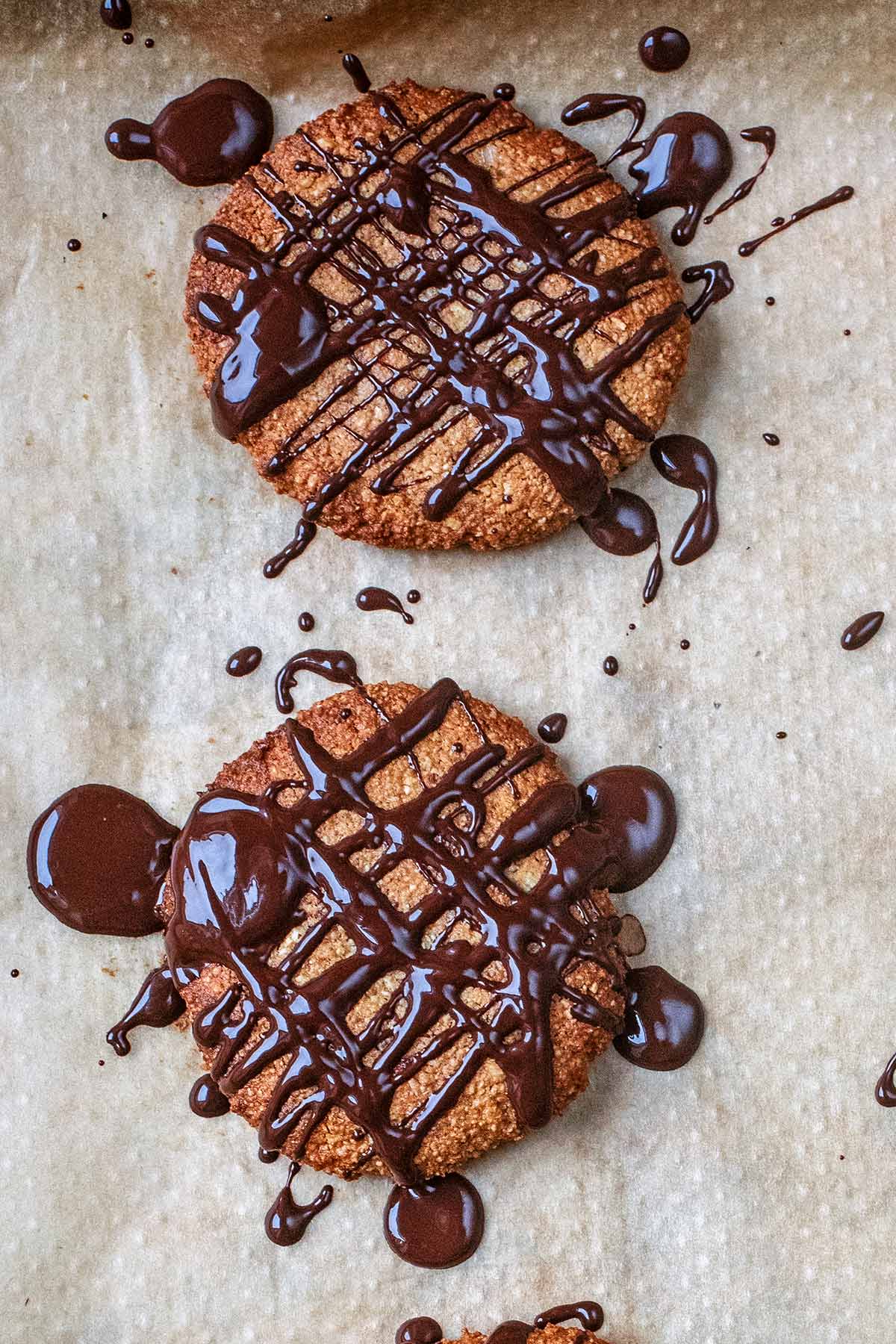 Two gingernut biscuits with melted chocolate drizzled over them.
