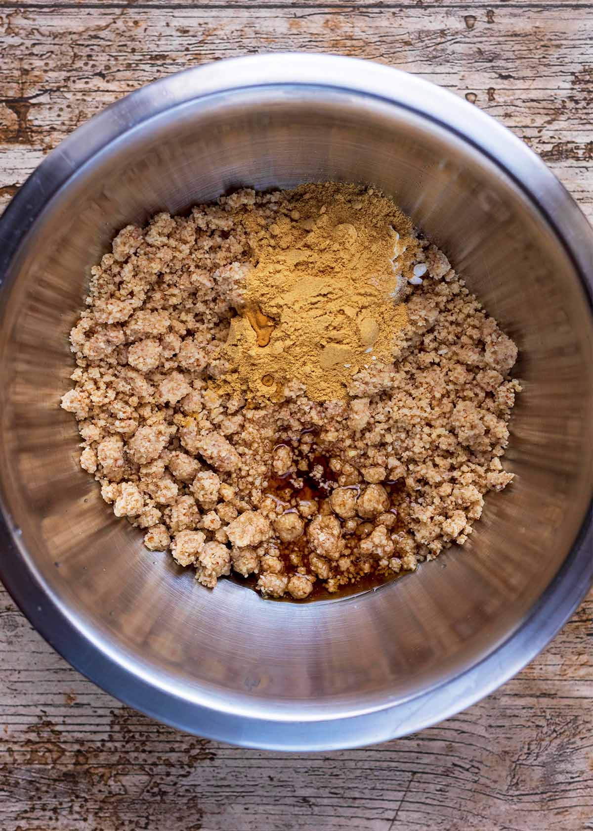 A large mixing bowl containing ground nuts, maple syrup and ground ginger.