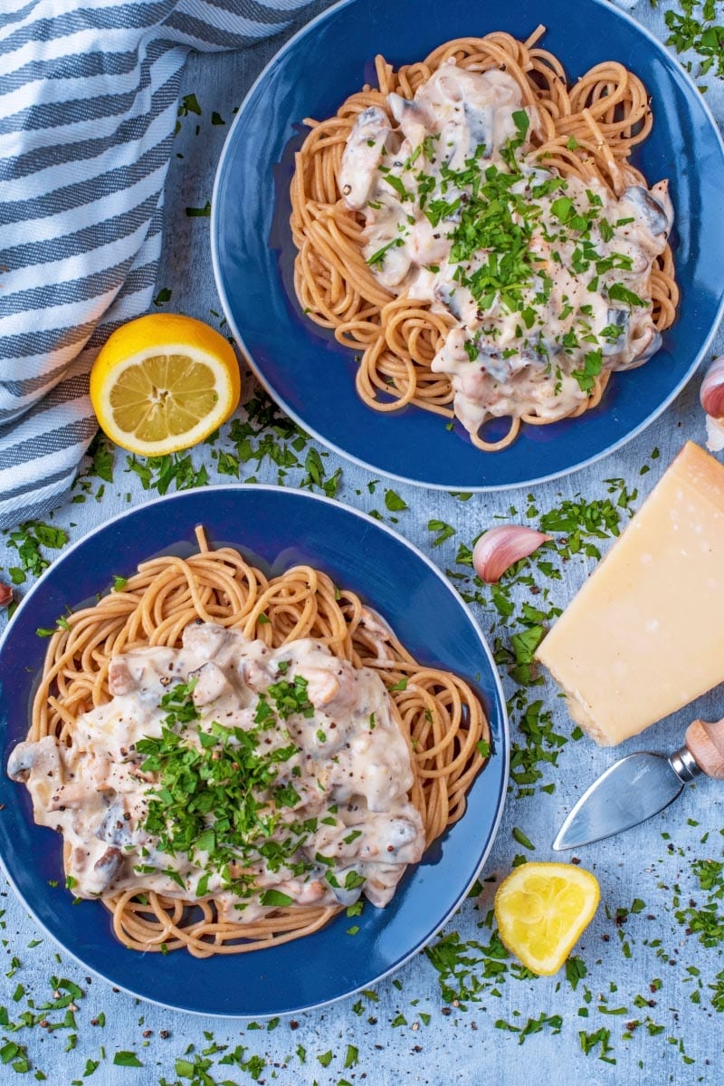 Two blue plates with Creamy Garlic Mushroom Pasta. A block of parmesan and lemon wedges sit next to them.