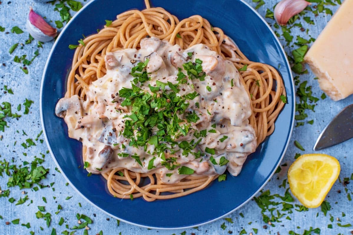 A blue plate with creamy mushroom pasta on it.