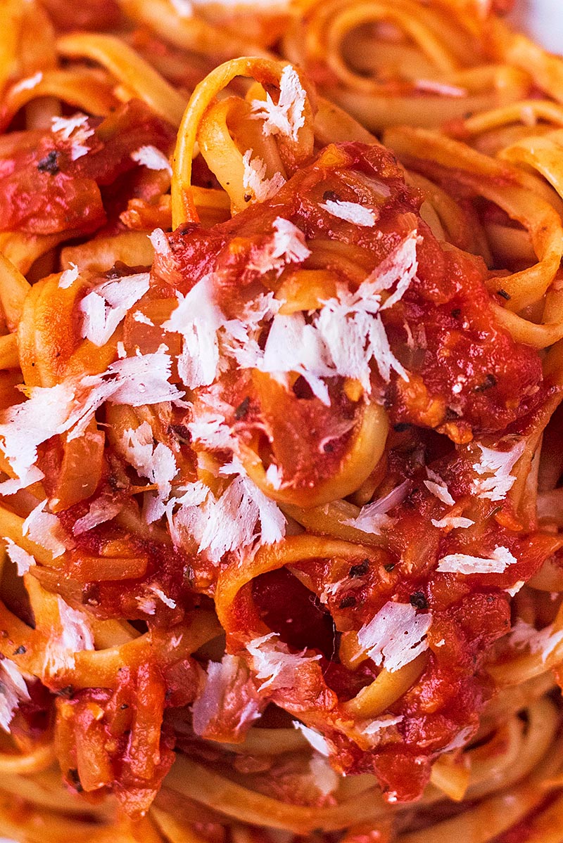 Parmesan shavings on top of pasta in a tomato sauce.