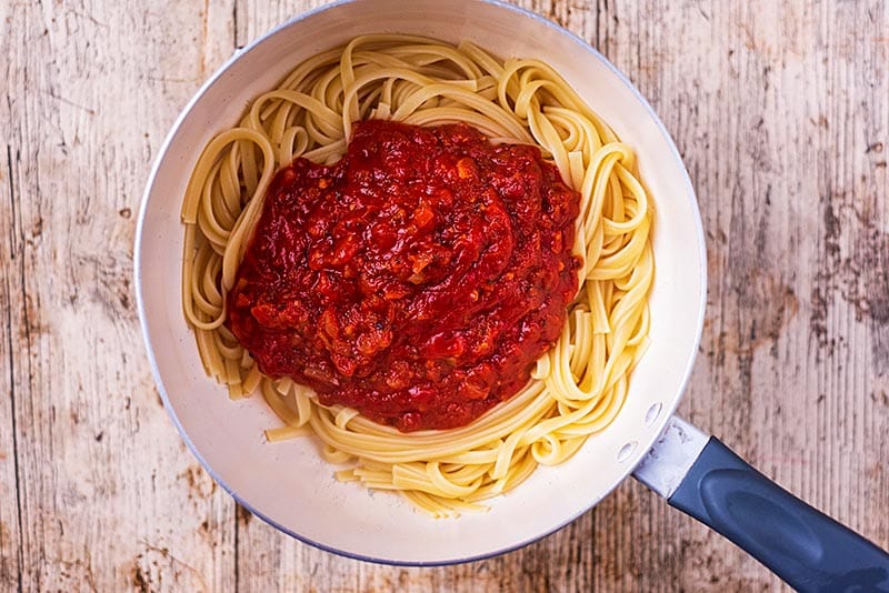 a saucepan containing cooked tagliatelle and tomato pasta sauce.