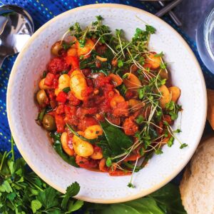 Spanish Bean Stew in a bowl next to a spoon, glass of water and slices of bread