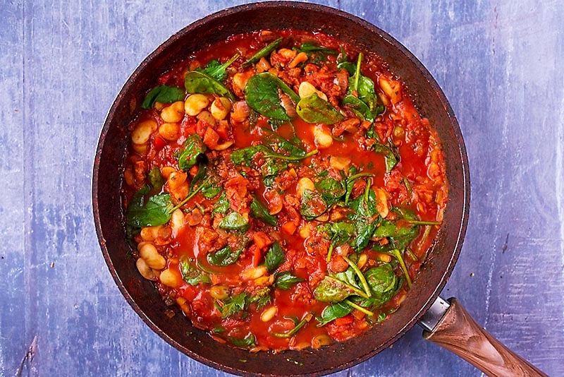 Spanish Bean Stew with wilted spinach cooking in a frying pan.