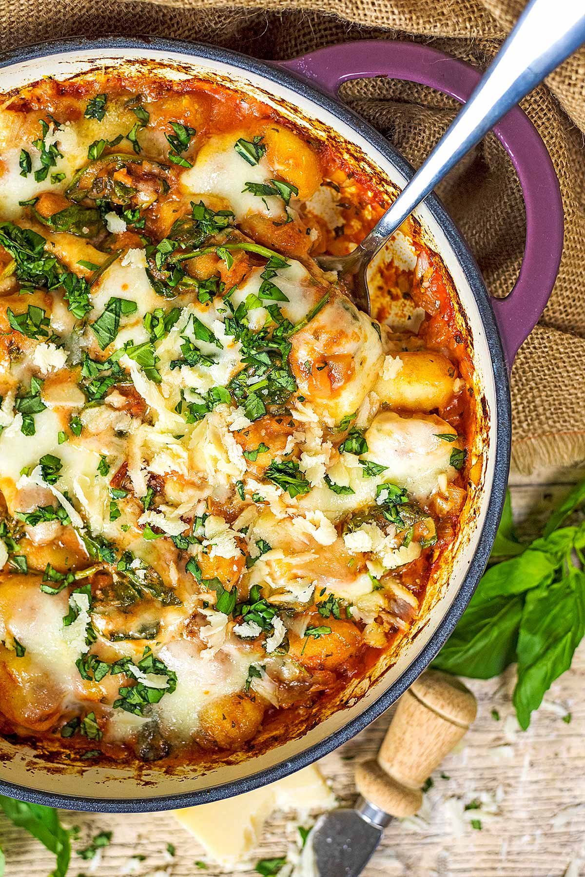 A baking dish full of cheesy gnocchi bake with a spoon in it.