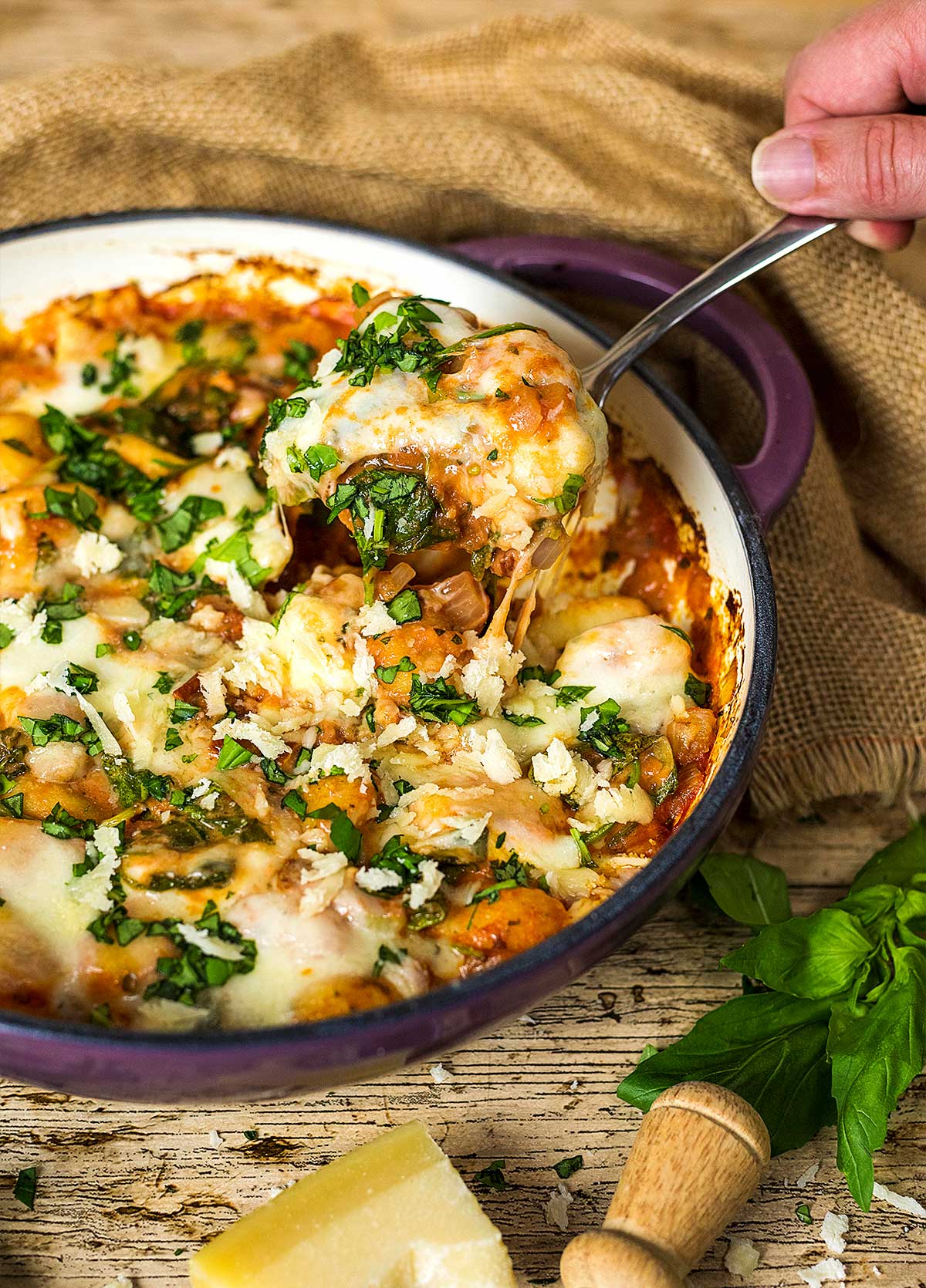 A hand spooning some gnocchi bake out of a baking dish.