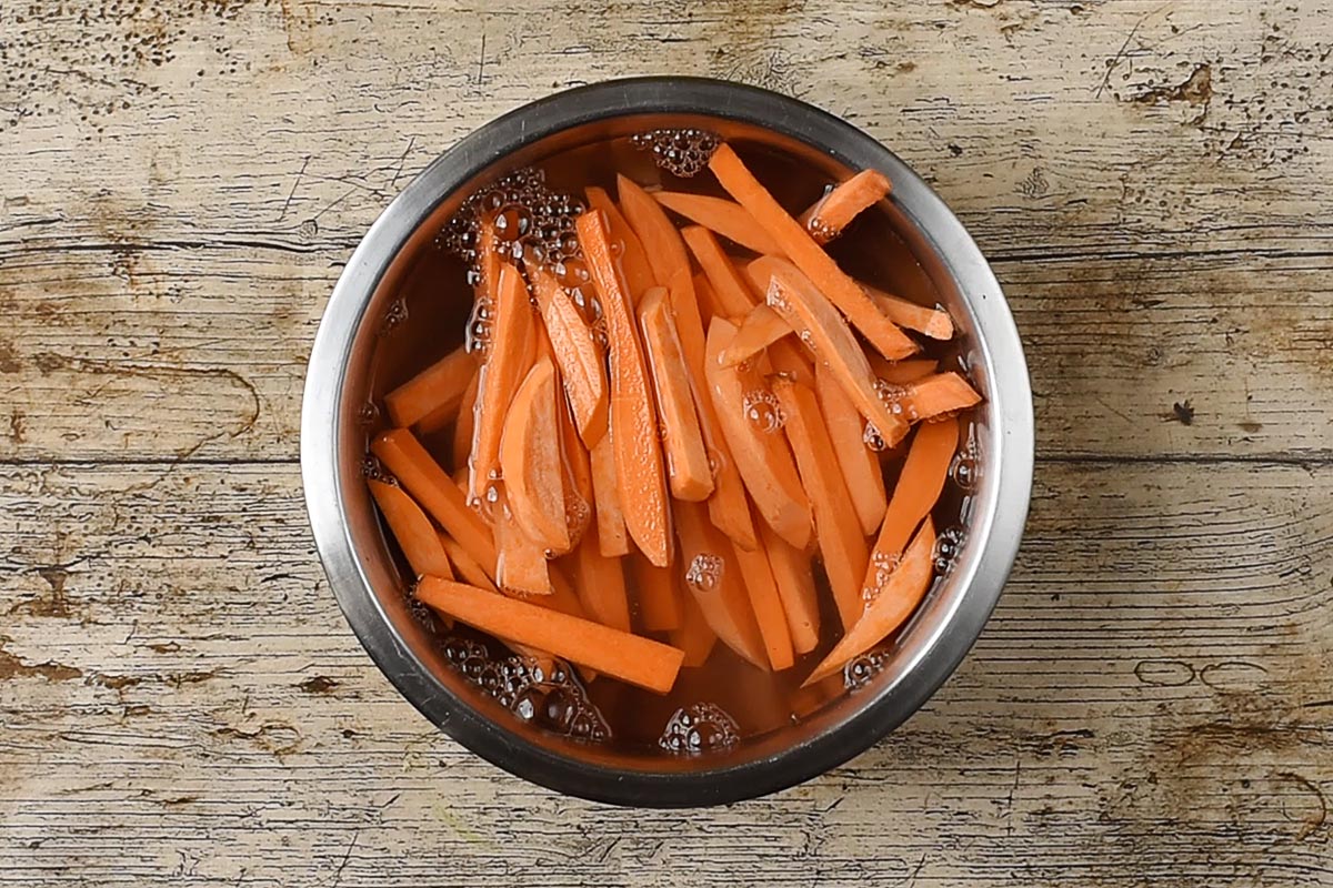 Uncooked sweet potato fries in a bowl of water.