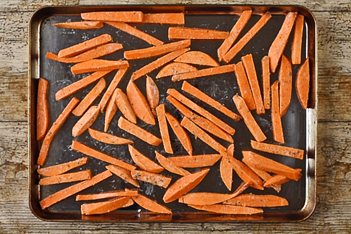 A large baking sheet with cut lengths of sweet potato on it.