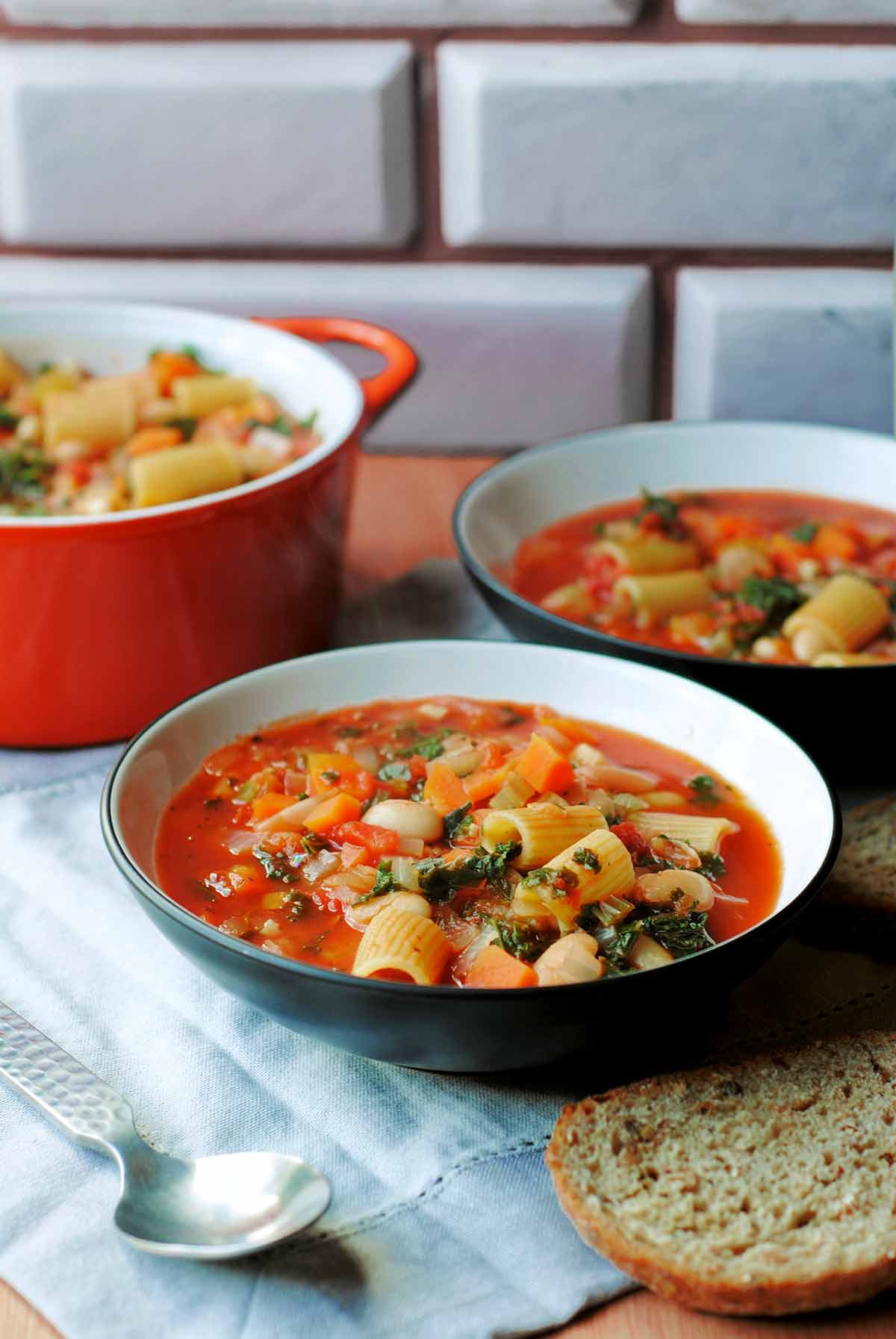 Two bowls of pasta soup in front of a tiled wall.