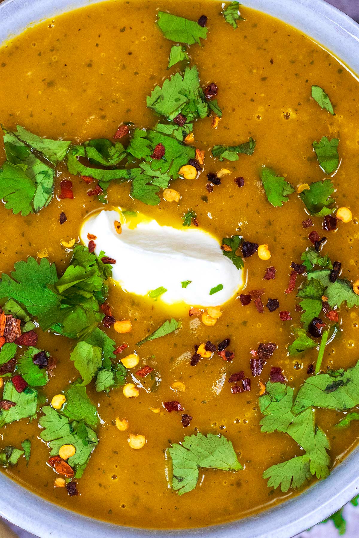 A bowl of soup topped with a dollop of cream, chopped coriander and chilli flakes.