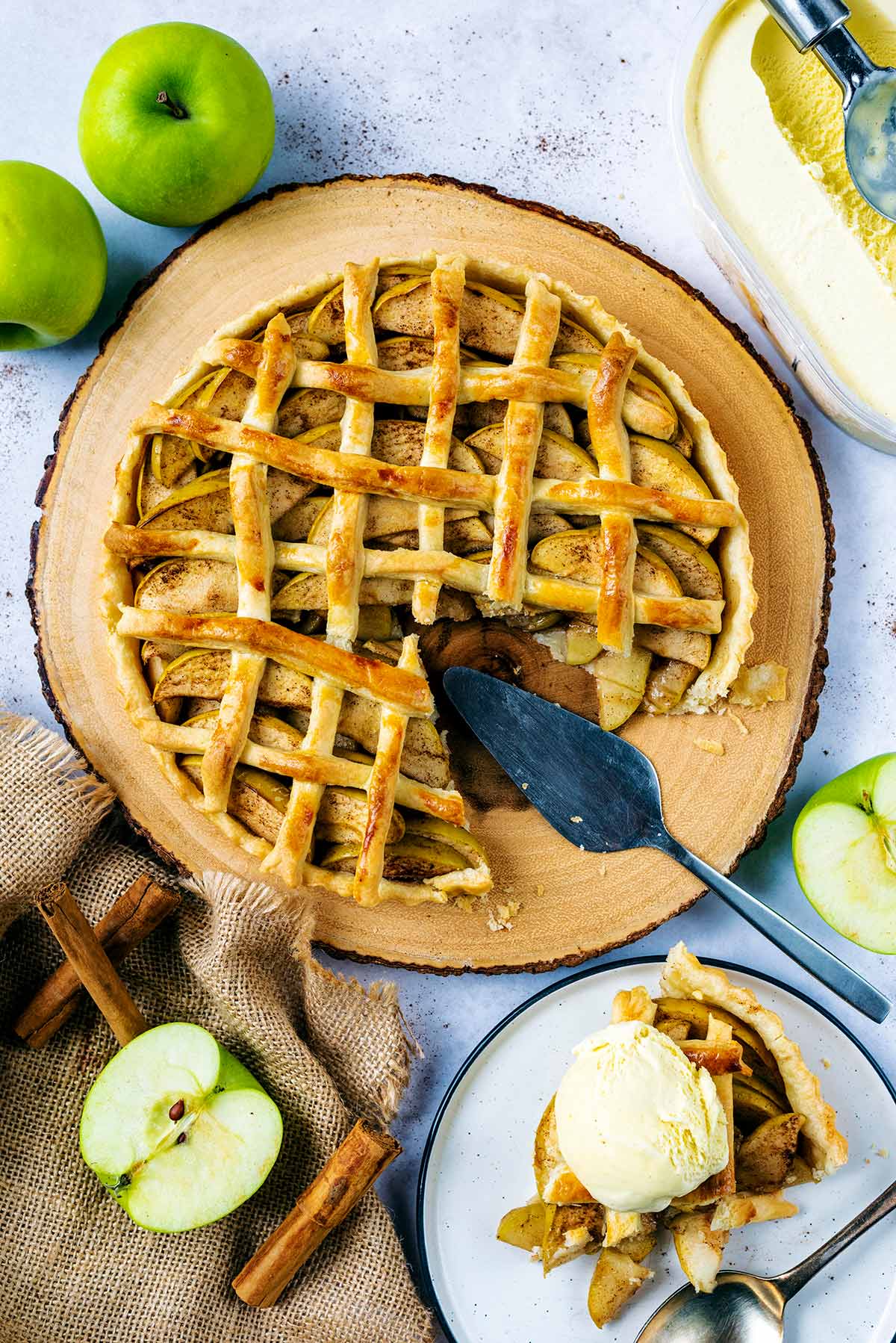 An apple pie with a slice removed, which is on a plate with a ball of ice cream.