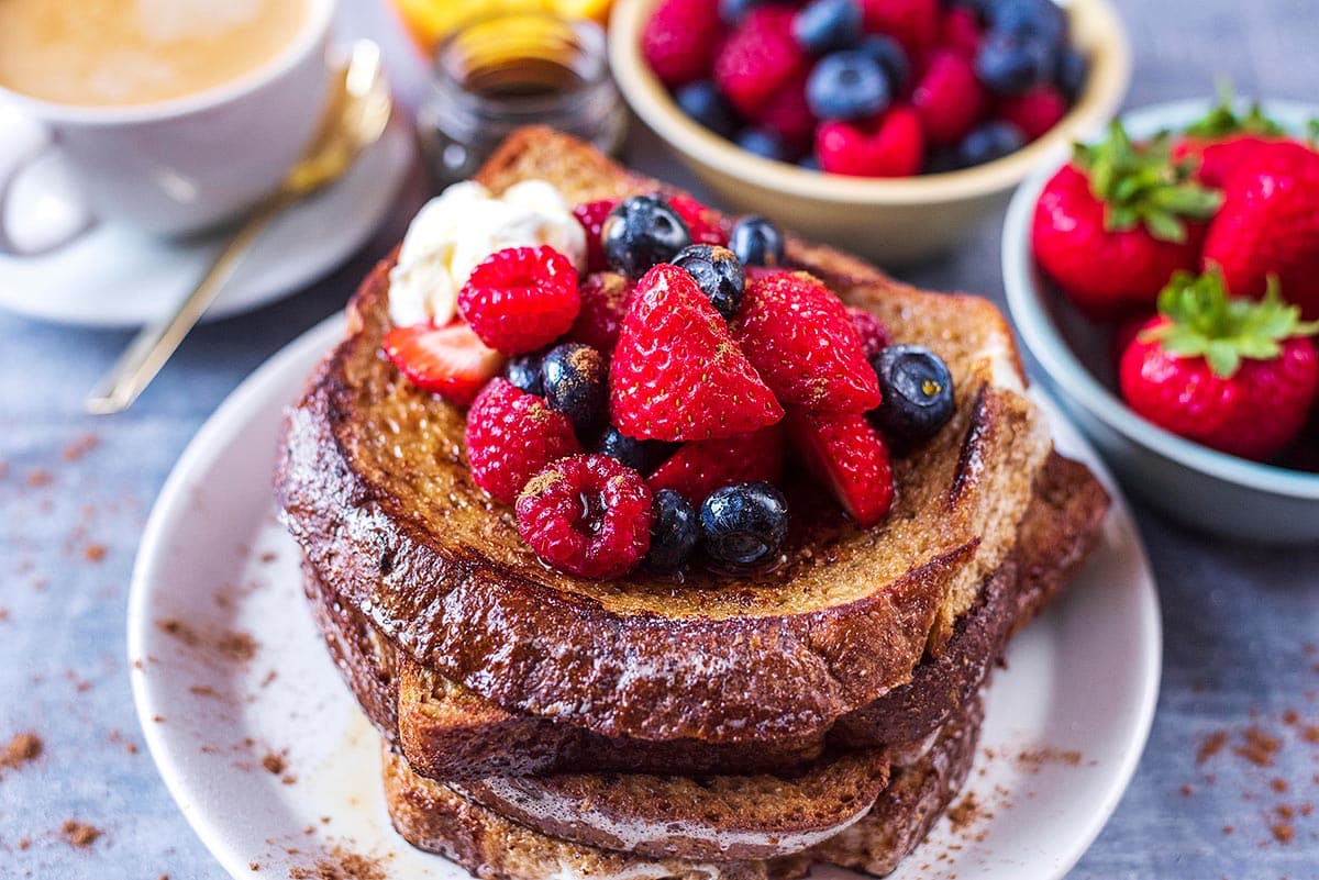 A stack of french toast topped with strawberries, raspberries and blueberries