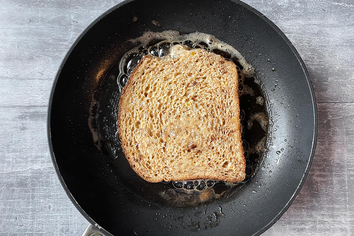 A slice of French toast cooking in a frying pan