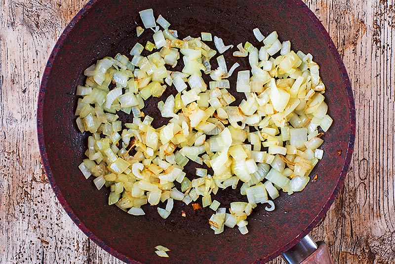 A frying pan with chopped onions cooking in it.
