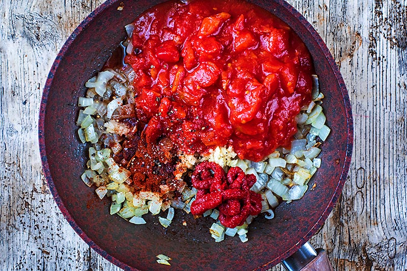 Chopped onions, chopped tomatoes, tomato paste and spices in a frying pan.