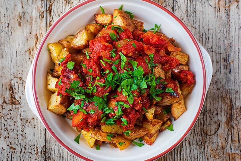 Cubes of cooked potato covered in a tomato sauce and chopped herbs.