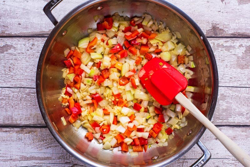 A large pan containing onions and red bell pepper cooking.