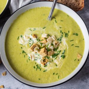 A bowl of asparagus soup topped with cream, croutons and Parmesan