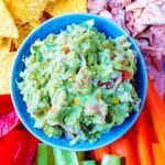 The best guacamole surrounded by sliced vegetables and tortilla chips.
