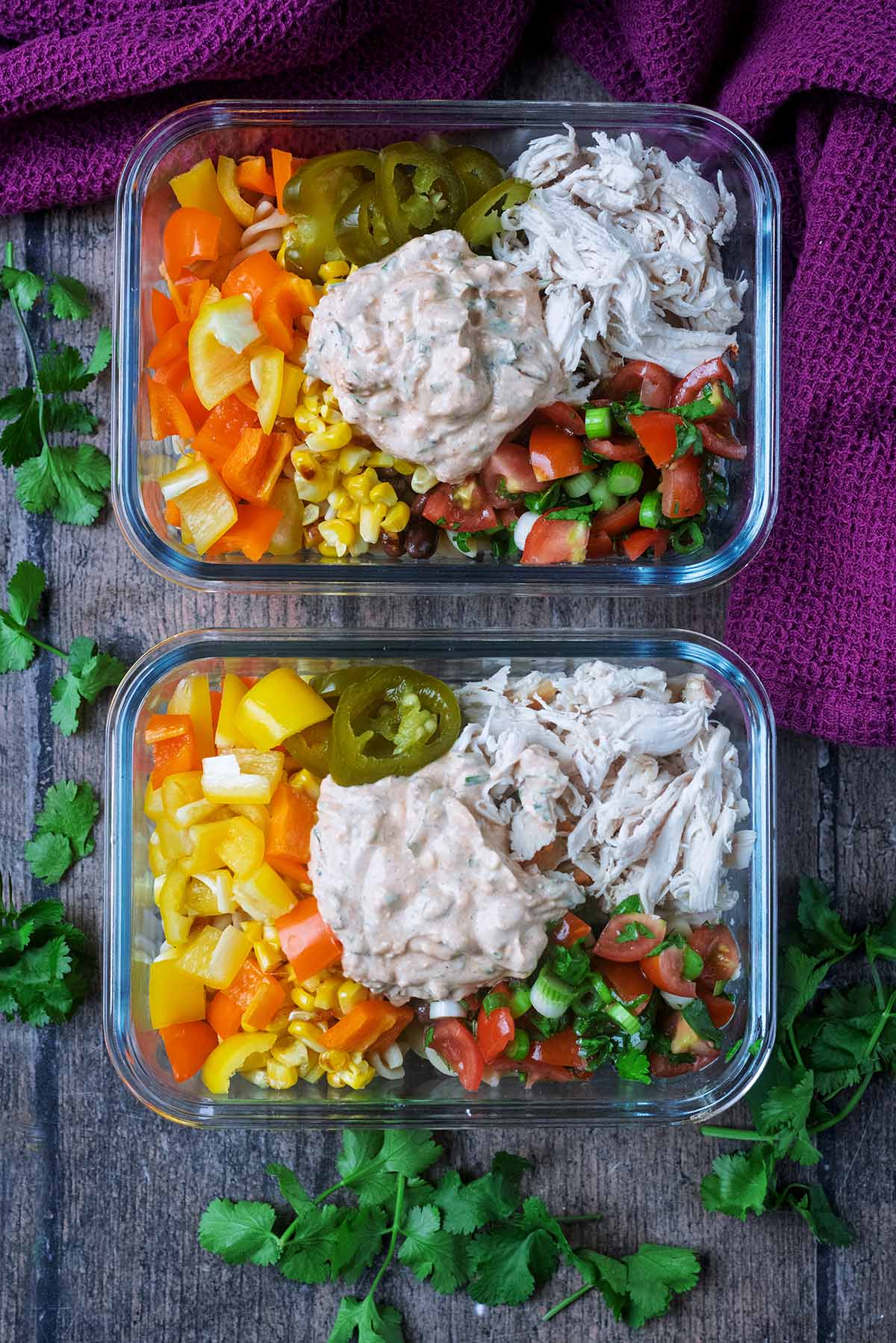 Two glass containers containing a pasta salad topped with a creamy dressing.