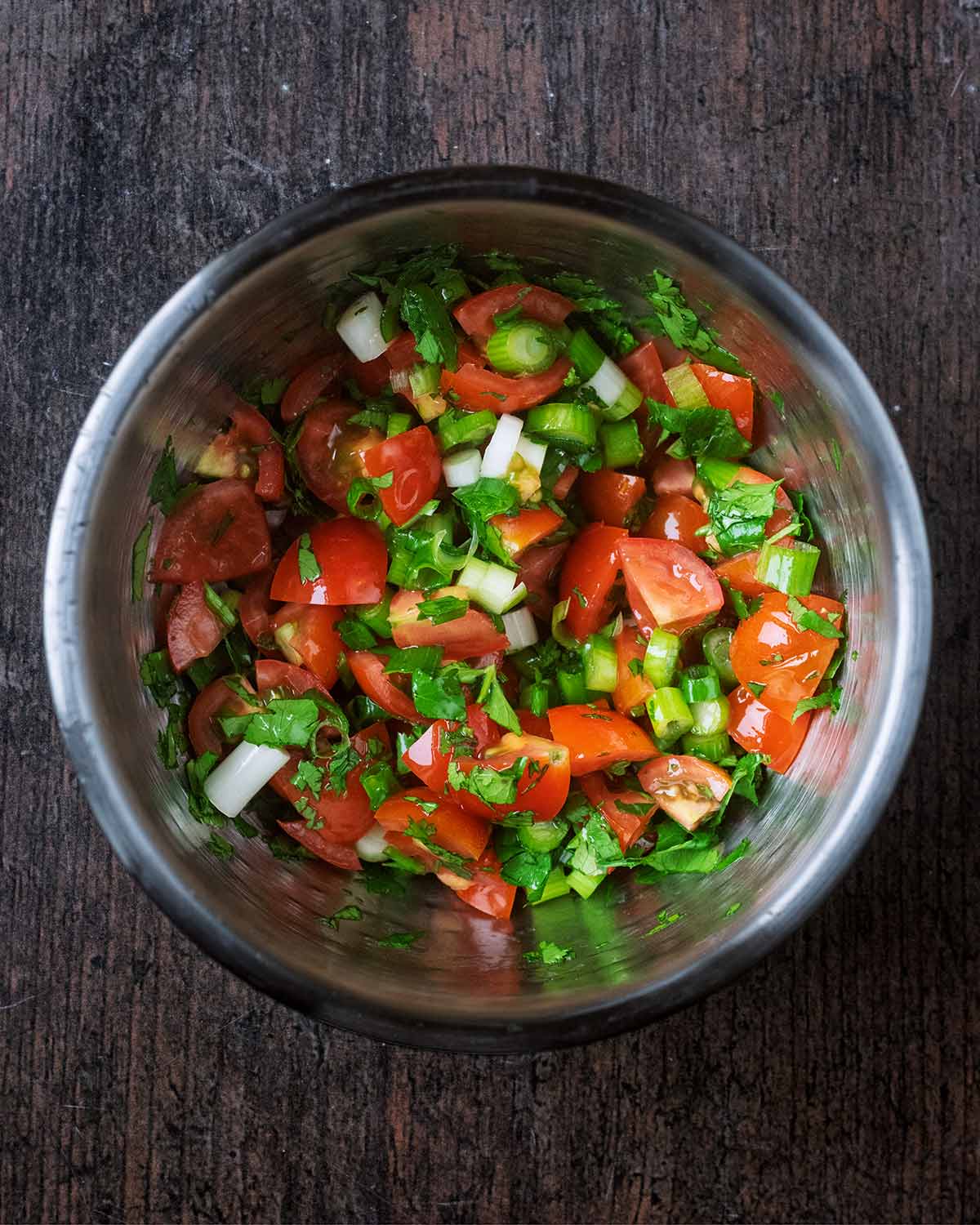 Chopped tomatoes, sliced spring onions and chopped coriander mixed in a bowl.