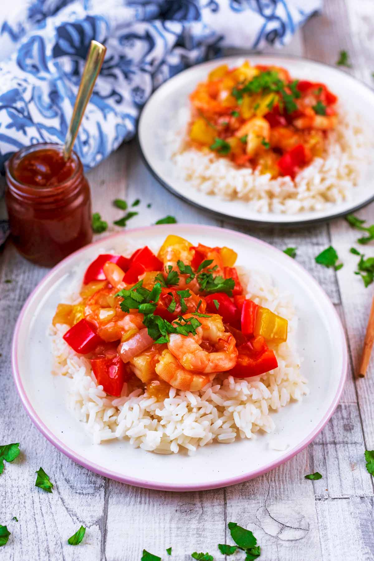Prawns (shrimp) in a sauce on top of rice next to a small jar of sauce.