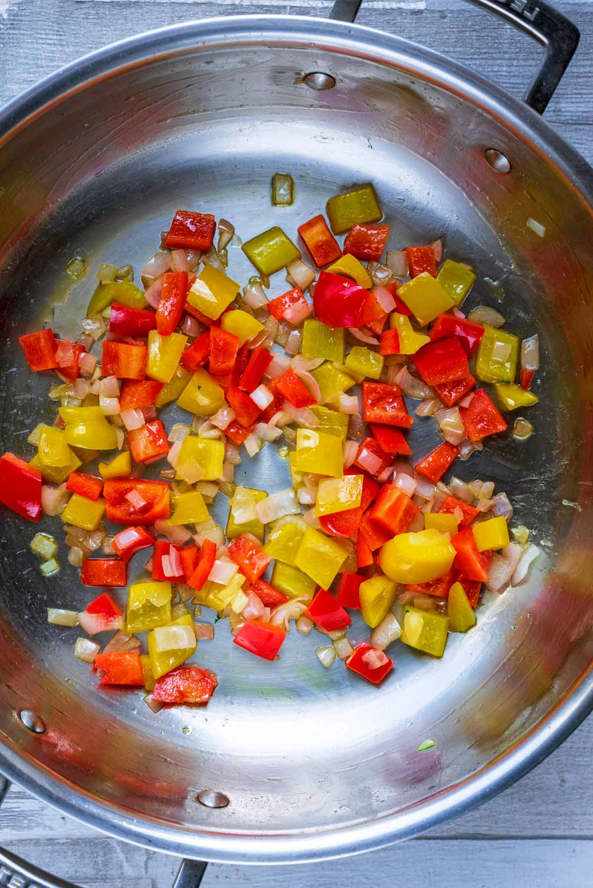 A large silver pan with chopped onion and red and yellow peppers cooking in it.