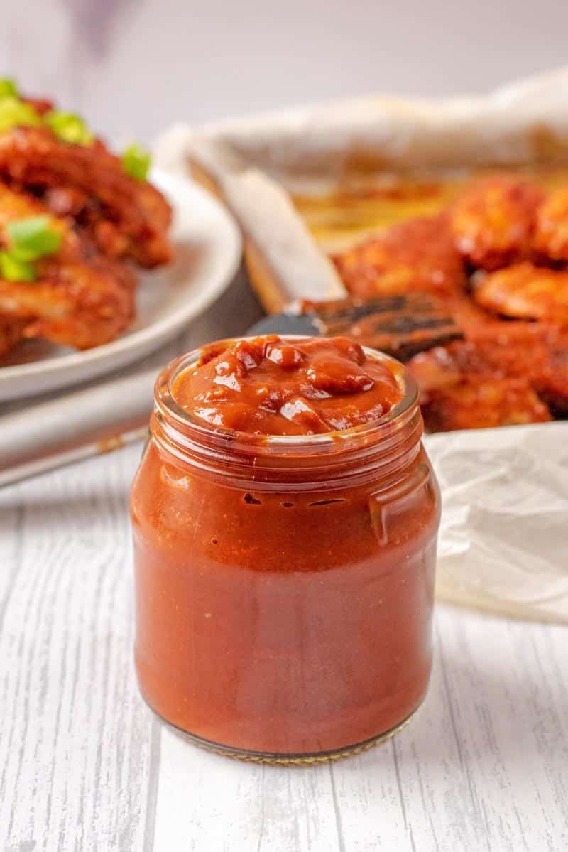 A jar of bbq sauce in front of a plate of chicken wings.