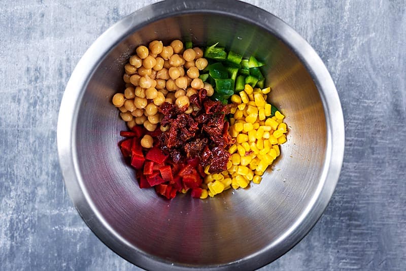 A mixing bowl containing chickpeas, chopped peppers, sun dried tomatoes and sweetcorn.